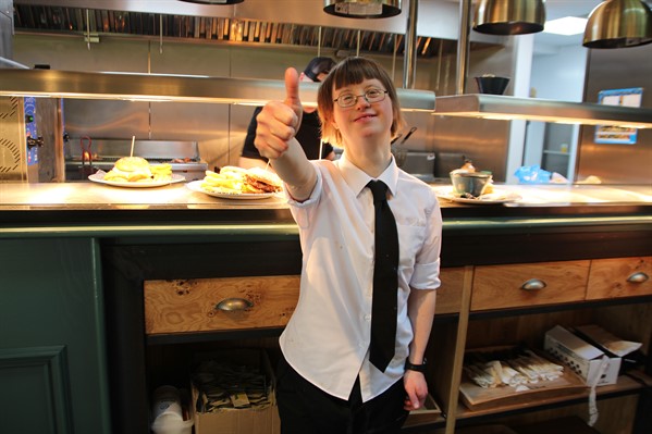 Smiling young woman with learning disabilities working as a waitress giving thumbs up