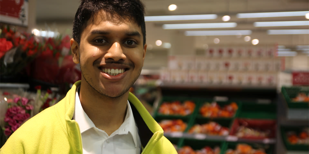 Young man wearing bright yellow jacket smiling in a supermarket