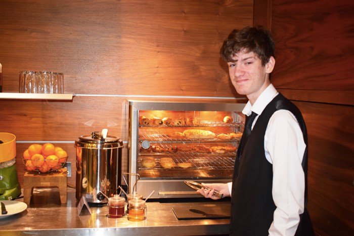 Young man in hotel uniform standing at a hotel breakfast counter