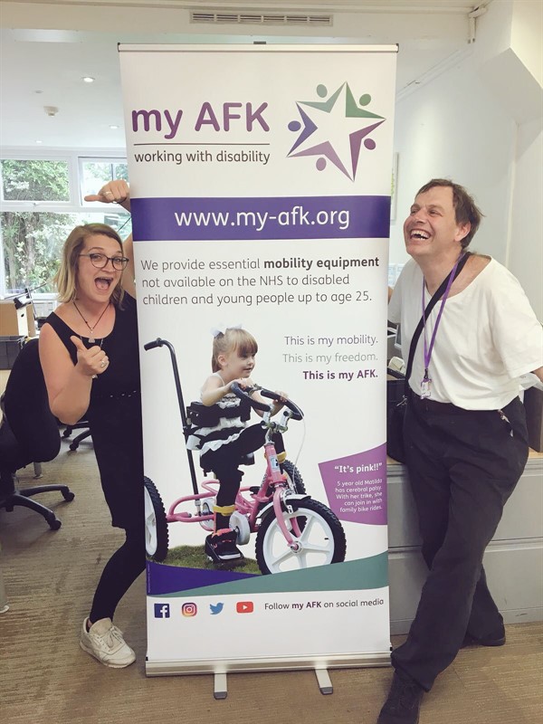 Caroline and Ben standing either side of a new pop-up banner for my AFK, featuring a young girl on a new pink trike