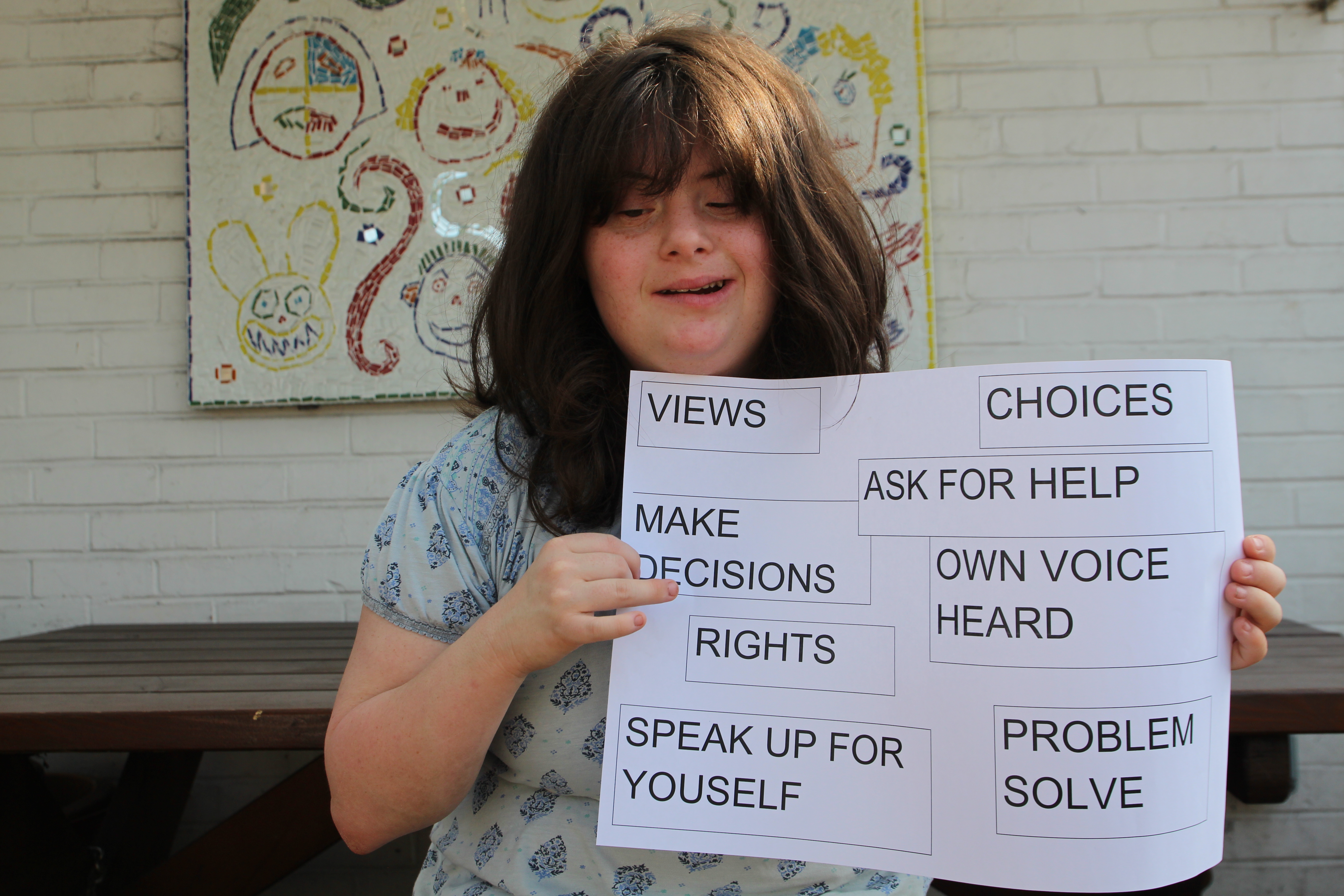 Young woman with learning disabilities holding a sign with different words showing what advocacy means