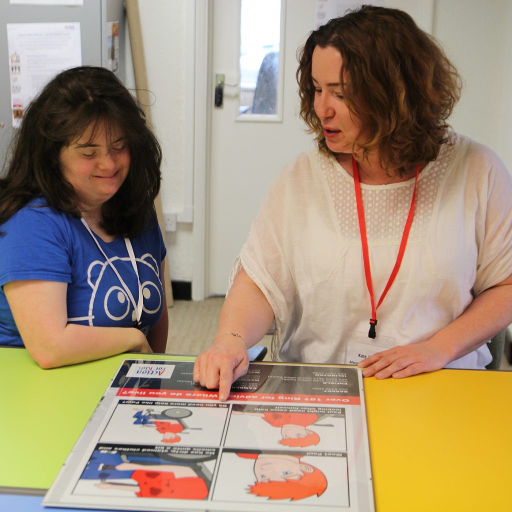 A woman showing a girl with learning disabilities a poster on a table