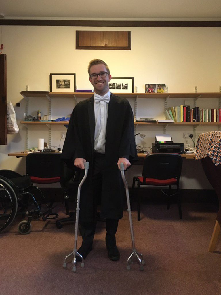 Jamie Green standing in matriculation robes with mobility aid walking sticks.