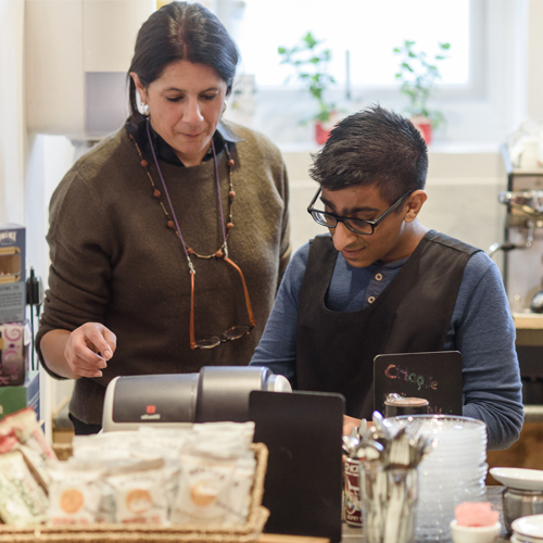 Woman helping young man with learning disabilities learn how to use a cafe till