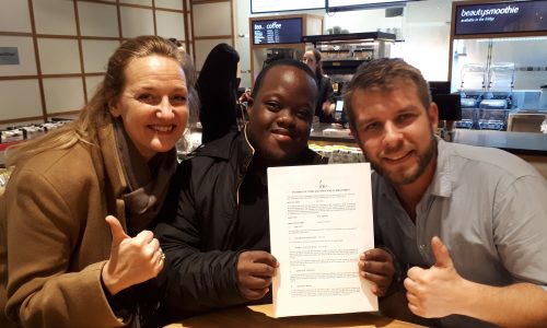 A young man with Down Syndrome with his managers, holding his work contract in an Itsu sushi resturant