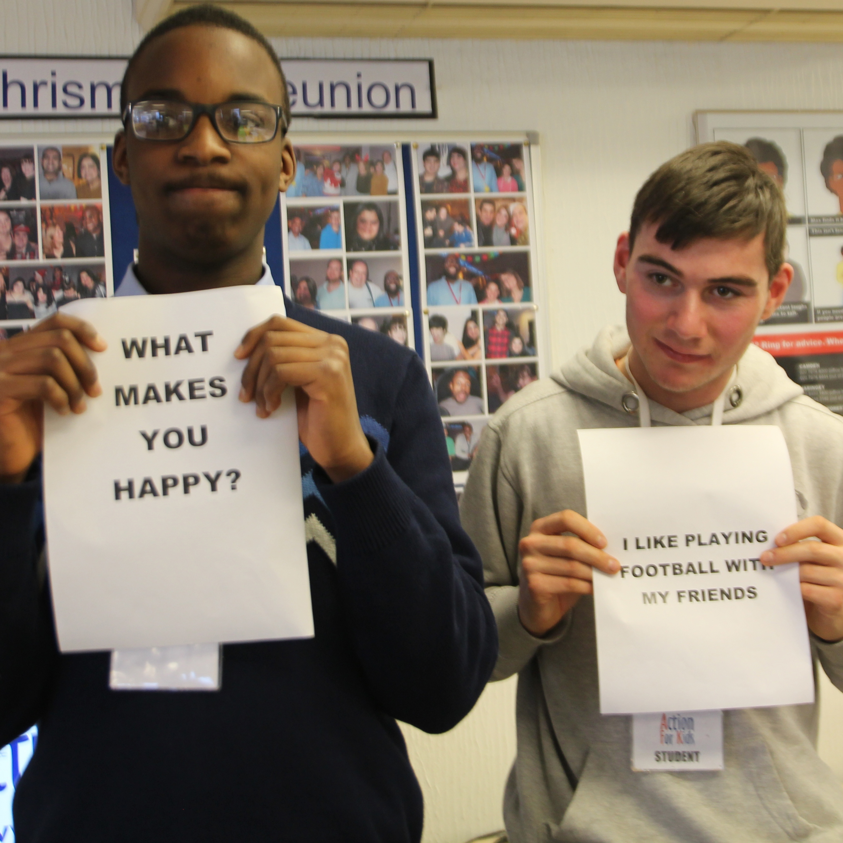 two people are holding signs, one says "what makes you happy?" the other says "I like playing football with my friends"